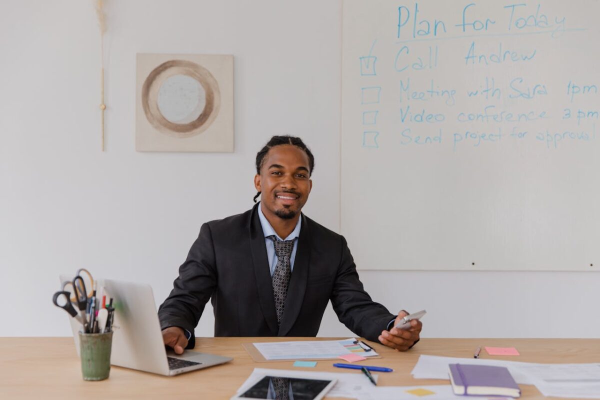 Professional man with braided hair working on a laptop in a modern office.