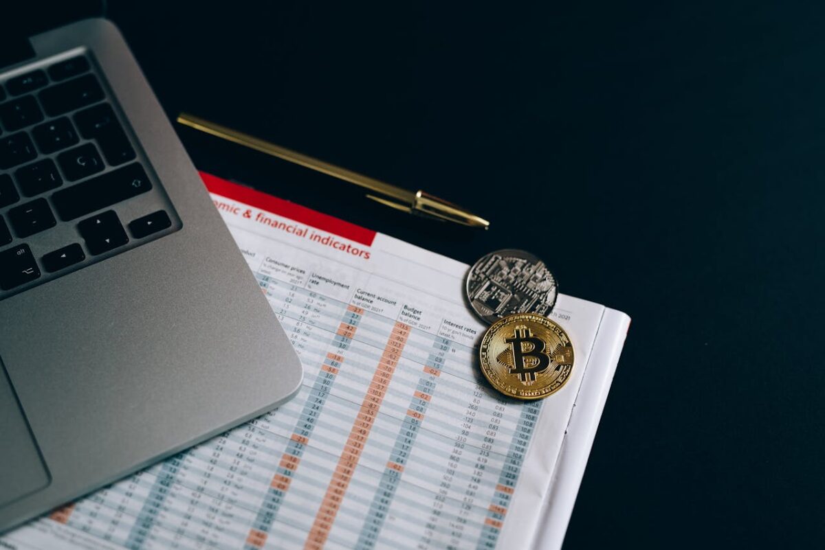 Bitcoin and cryptocurrency coins placed on a financial document next to a laptop.